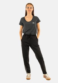 Zwart gestreepte t-shirt met ronde hals en logo, gecombineerd met zwarte joggers met streepjes aan de zijkant. Tan sneakers maken de look compleet.