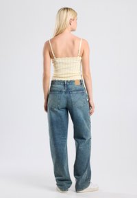 Light yellow, textured knit tank top with thin straps paired with loose, faded blue denim jeans. Jeans feature back pockets and a square label.