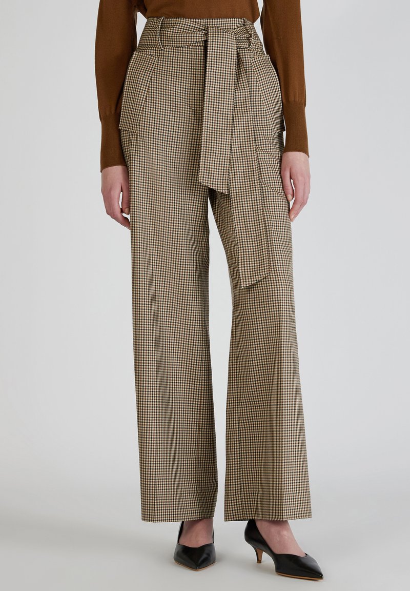 Geruite broek met brede pijpen in bruin en crème stof, voorzien van een riem in de taille en zijzakken, gecombineerd met zwarte puntige hakken.