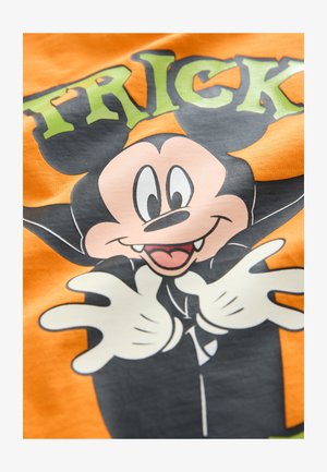 Oranžinė marškinėliai su animaciniu herojumi, vilkinčiu juodą apsiaustą, baltas pirštines ir turinčiu žaismingą išraišką, ant oranžinio fono.