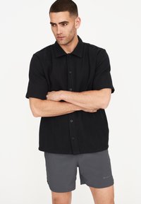 Camicetta nera a maniche corte con bottoni, in tessuto testurizzato e colletto, abbinata a pantaloni corti grigi con dettagli di logo.
