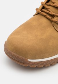 Scarpa sintetica marrone con una trama liscia, punta rotonda, suola in gomma con grip testurizzato e lacci dello stesso colore.