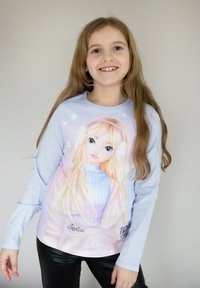 Camicia a maniche lunghe di colore azzurro chiaro con un personaggio stampato dai capelli biondi, che indossa cuffie e presenta dettagli di colore rosa chiaro nel design.