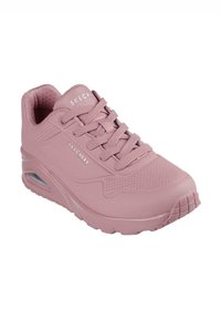 Zapatilla Skechers de color rosa claro, con material suave, puntera redonda, acentos perforados y suela texturizada con un talón de aire.