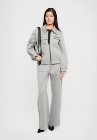 Gray sweatshirt with zip closure and patch details, paired with matching flared sweatpants. Model holds a textured black handbag.