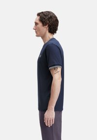 Camiseta de manga corta azul marino con cuello de canalé y acentos en las mangas. Tejido de algodón, estilo ajustado, con un pequeño logotipo bordado en el pecho.