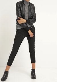 Černá kožená bomber bunda přes šedý rolák, spárovaná s černými úzkými kalhotami a kotníkovými botami. Hladká textura a přiléhavý design.