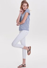 Lys blå kortærmet t-shirt parret med tætsiddende hvide ankel-lange jeans med sidelommer og brune sandaler med sorte accenter.