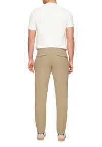 Lichtbeige op maat gemaakte broek met een slim fit, voorzien van achterzakken en een gladde textuur, gecombineerd met een wit shirt met korte mouwen.