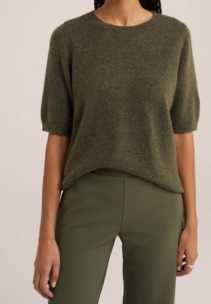Zielony, krótkosleeowy sweter z dzianiny o okrągłym dekolcie i luźnym kroju, zestawiony z dopasowanymi zielonymi spodniami. Miękka faktura i swobodny design.