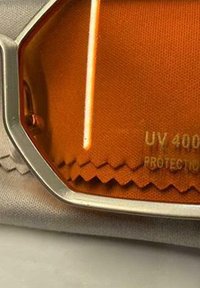 Nahaufnahme einer orangefarbenen UV-400-Schutzsonnenbrillenglaslinse mit silbernem Rahmen, die auf einem grauen Mikrofasertuch liegt.