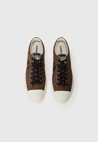 Bruine canvas sneakers met zwarte veters en steraccenten. Witte rubberen neuskap en zool. Logo op de tong met de tekst "Converse Star."