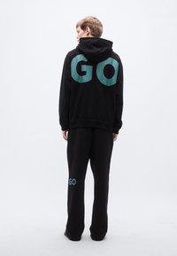Μαύρο φούτερ με κουκούλα και τιρκουάζ γράμματα "GO" στην πλάτη, σετ με αντίστοιχη φόρμα που διαθέτει την ίδια λεπτομέρεια κειμένου. Μαλακό ύφασμα, άνετη εφαρμογή.