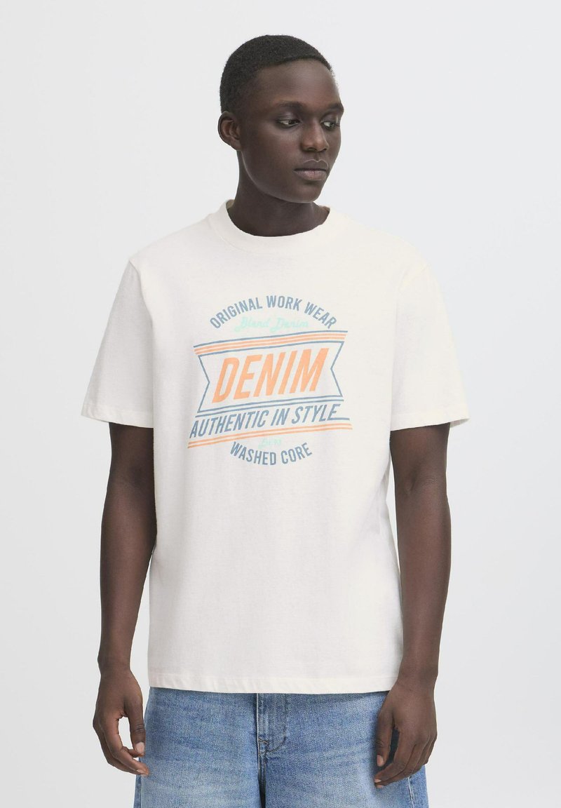 Off-white kokvilnas T-krekls ar īsām piedurknēm, kas rotāts ar grafisku zīmējumu zilā un korallkrāsā ar uzrakstu "DENIM AUTHENTIC IN STYLE."