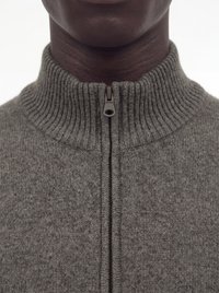 Gros plan d'une personne portant un pull en maille côtelée grise avec un col montant zippé.