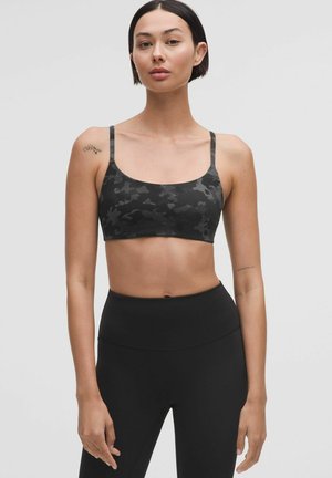 Sutien sport de camuflaj negru cu bretele subțiri și decolteu rotund, asortat cu colanți negri cu talie înaltă. Material neted și elastic.