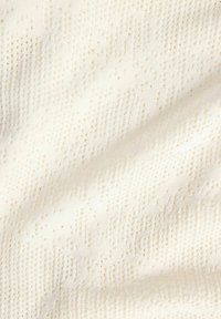 Gros plan sur un tissu texturé blanc cassé avec un motif géométrique subtil et de petites perforations dans un matériau doux et tissé.
