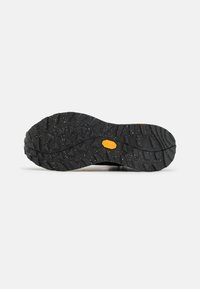 Suola di scarpa nera con scanalature triangolari e rettangolari profonde, con il logo giallo Vibram al centro su uno sfondo bianco.
