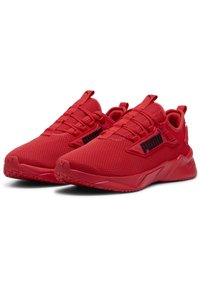 Baskets de sport rouges avec une tige en maille, fermeture à lacets et un logo noir audacieux sur le côté. Semelle en caoutchouc à crampons pour une meilleure traction.