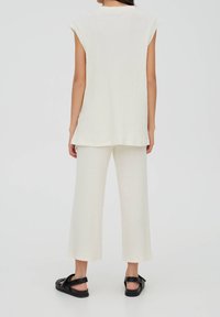 Conjunto de color crema claro con textura acanalada que incluye una blusa sin mangas y pantalones acampanados, confeccionado en una suave tela texturada y sandalias planas negras.