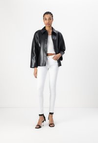 Μαύρο ψεύτικο δερμάτινο μπουφάν με γιακά, μπροστινά κουμπιά, φορεμένο πάνω από ένα λευκό crop top και συνδυασμένο με λευκά skinny τζιν και μαύρες γόβες.