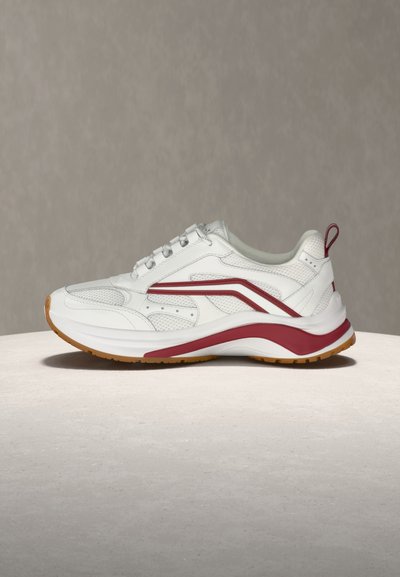 Λευκό αθλητικό αθλητικό παπούτσι με κόκκινες λεπτομέρειες, διχτυωτές επιφάνειες, παχιά σόλα και εξωτερική σόλα σε χρώμα τσίχλας, σε ουδέτερη επιφάνεια και φόντο.