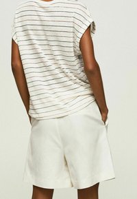 Gestreepte T-shirt met korte mouwen in crème kleur, met zwarte en bruine lijnen, gecombineerd met witte, losse shorts met zijzakken.