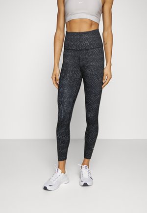 Sorte leggings med et struktureret mønster og høj talje, parret med en grå sports-bh og hvide træningssko.