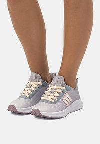 Zapatillas de running ligeras en gris con parte superior de malla. Presentan acentos en naranja pálido, un acabado texturizado y una suela blanca flexible con una base morada.