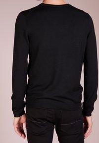 Svart långärmad tröja med rund halsringning, stickad textur och ribbade ärmslut, kombinerad med åtsittande svarta byxor med bakfickor.