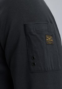 Zwarte langemouwen shirt met een borstzak featuring een label en twee zwarte oogjes. Gemaakt van glad, gestructureerd materiaal.