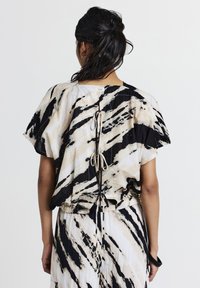 Donna con capelli scuri raccolti in una coda di cavallo, che indossa un top e una gonna con un motivo astratto in bianco, nero e beige, mostrata di spalle.