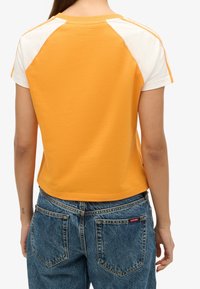 Camiseta de manga corta de corte relajado en algodón amarillo brillante con mangas raglán blancas. Presenta un cuello redondo y un detalle de marca minimalista en la parte posterior.