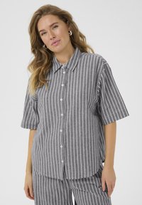 Chemise à rayures grises avec des manches courtes, comportant des rayures blanches verticales et une coupe décontractée. Boutons blancs simples sur le devant.