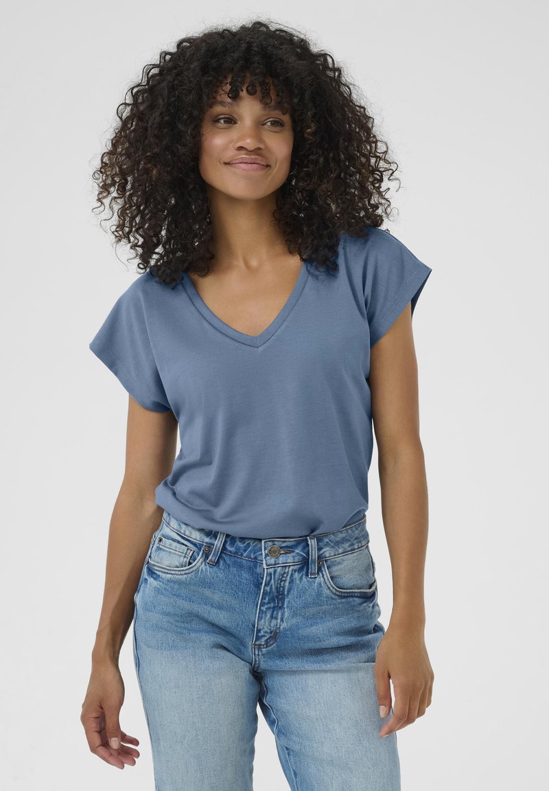 T-shirt blu a collo a V con maniche corte arrotolate, realizzato in tessuto morbido. Abbinato a jeans in denim chiaro con una vestibilità classica.