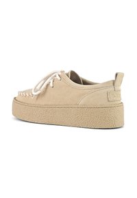 Beige suede sneaker with a textured rubber sole, lace-up front, and stitched design along the toe. Subtle branding on the heel.