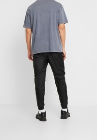 Grå bomulls t-shirt med korta ärmar, kombinerad med svarta syntetbyxor. Byxorna har en tapered passform och elastiska manschetter vid anklarna.