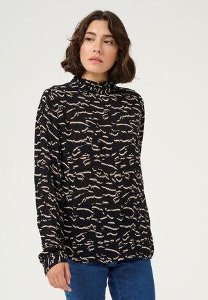 Top lungo nero a maniche, con una texture a costine, caratterizzato da un motivo astratto color crema chiaro e un collo alto. Indossato con jeans blu.