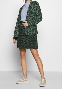 Blazer verde a fantasia abbinato a una gonna. Indossato sopra un maglione a coste di colore azzurro chiaro. Sneakers beige completano il look.
