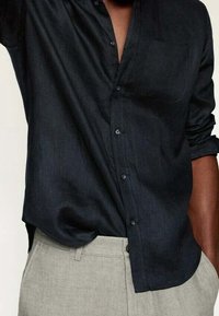 Chemise bleu foncé à boutons, fabriquée en tissu léger, avec une poche poitrine, des manches longues retroussées et une coupe décontractée.