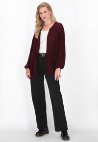 Burgundy malli neulecardigan leveillä hihoilla, avonainen etuosa, yhdistettynä korkeavyötäröisiin mustiin housuihin ja mustiin nilkkureihin.