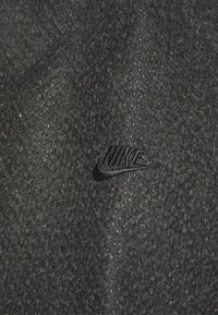 Tela negra con una superficie texturizada que presenta pequeñas perforaciones, incluye un logotipo de Nike en relieve sutilmente en negro.