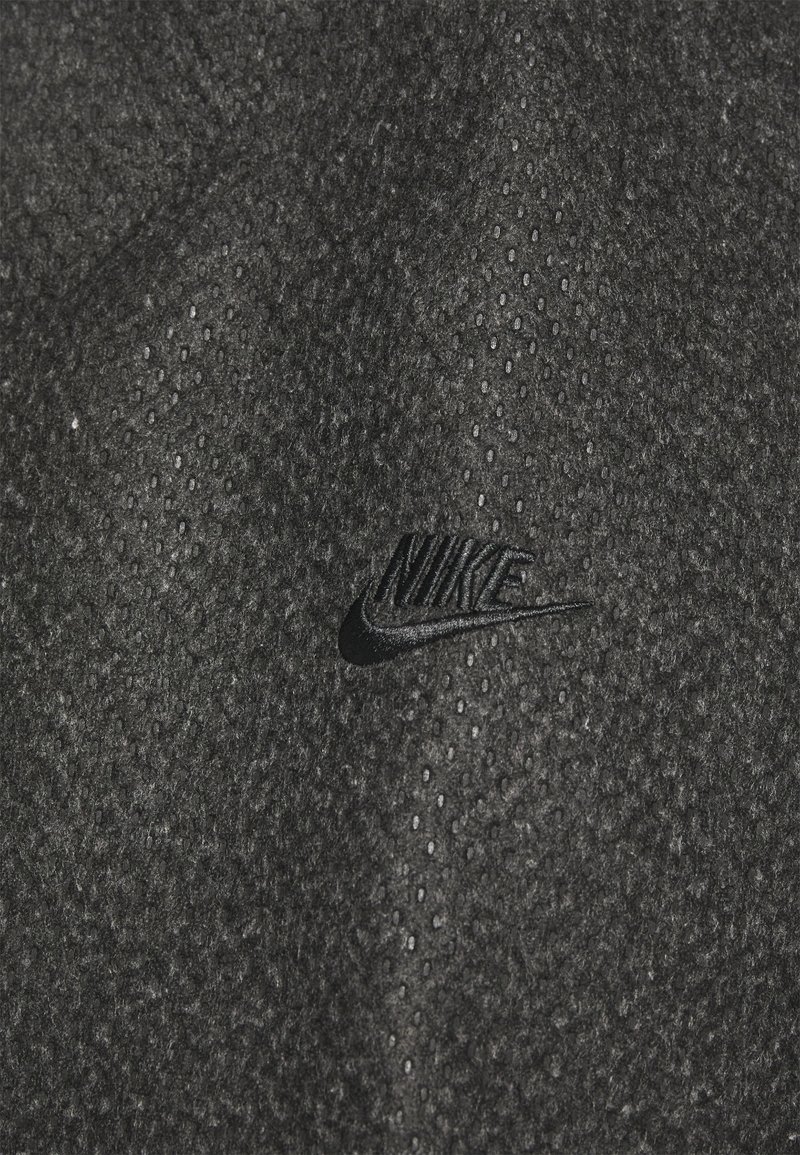 Tela negra con una superficie texturizada que presenta pequeñas perforaciones, incluye un logotipo de Nike en relieve sutilmente en negro.