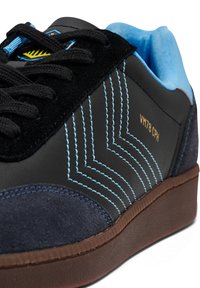 Sapatilhas de couro preto e camurça azul com costura azul contrastante, atacadores planos e sola de borracha castanha. Apresenta o texto "VM78 CPH."