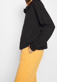 Felpa nera con scollatura arricciata, abbinata a pantaloni arancioni morbidi. Entrambi i capi sono casual, con maniche lunghe e una vestibilità comoda.