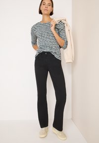 Jeans neri con vestibilità slim, abbinati a una camicia a maniche lunghe a strisce multicolori nei toni del verde, blu e bianco. Presenta maniche a 3/4 e una texture a coste.