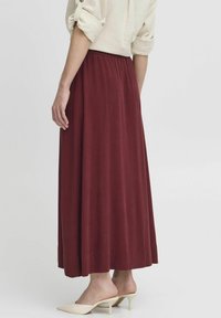 Fustă maxi bordeaux, confecționată dintr-un material moale, cu un brâu elastic și o siluetă fluidă. Asortată cu mule cu toc de culoare crem.