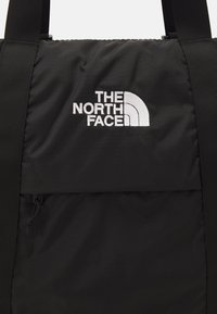 Mochila negra de nylon con una superficie texturizada, que cuenta con un bolsillo frontal, correas ajustables y un logo bordado en blanco en la esquina superior izquierda.