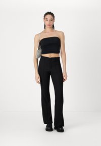 Top noir court sans bretelles avec texture froncée, associé à un pantalon noir évasé taille haute et des chaussures noires chunky. Petit sac à main en argent.