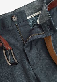 Pantaloni blu navy con un motivo testurizzato, dotati di zip, cintura in pelle marrone e fodera decorativa interna con piccole stampe floreali.